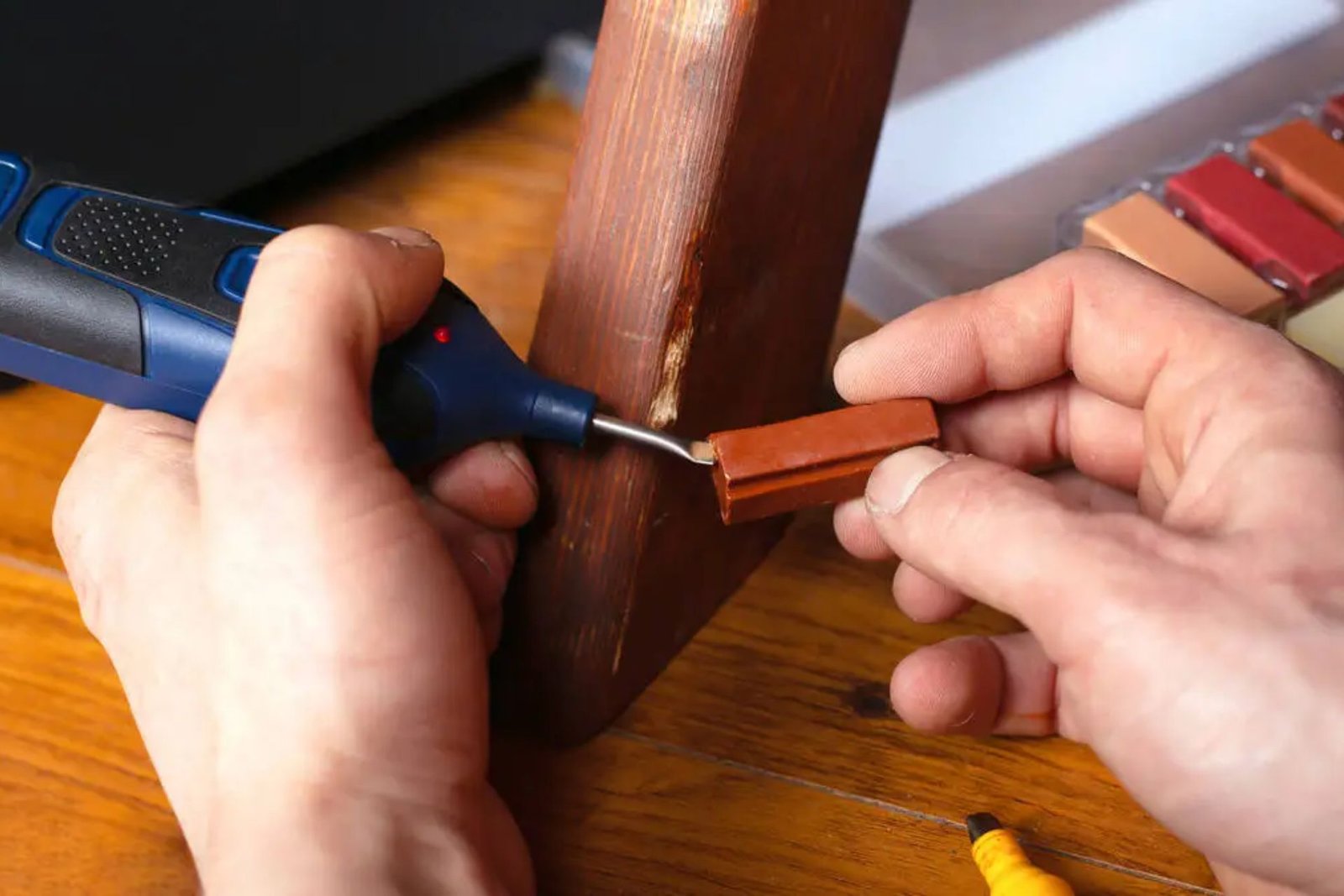 A person repairs a wooden chair using a power tool, focused on their task in a well-lit workshop environment.