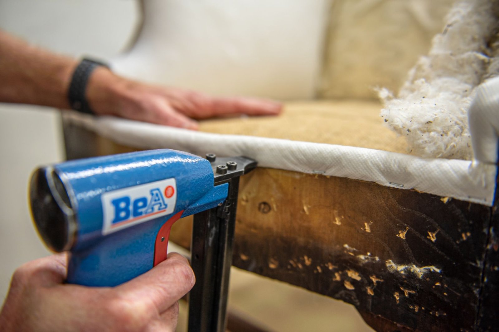 A man repairs a chair using a heat gun, focusing intently on the task at hand in a well-lit workshop.