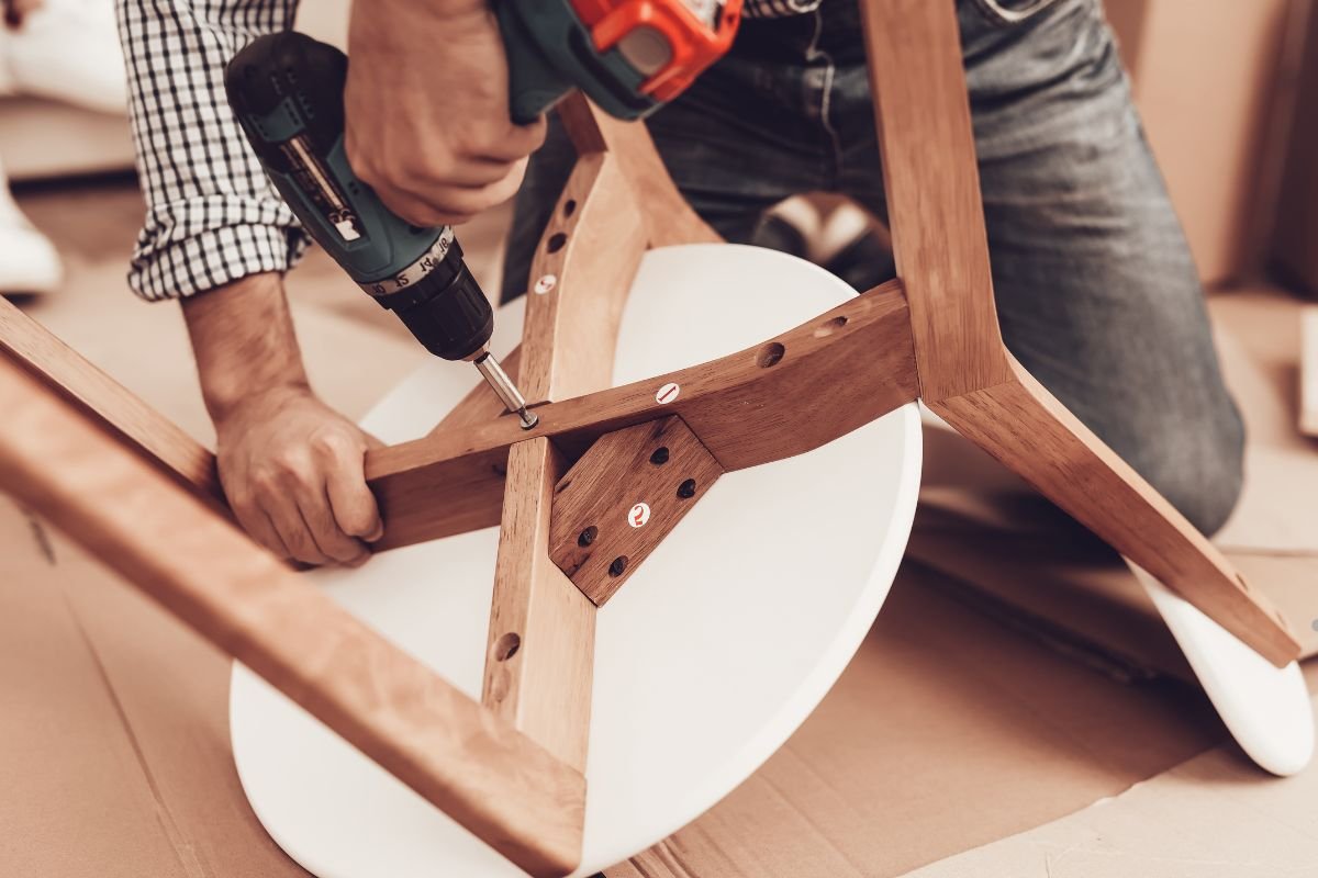 A man operates a drill while repairing a chair as part of a furniture repair service.