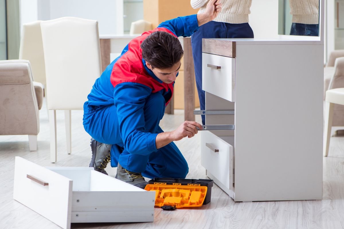 A man wearing blue overalls works on fixing a cabinet, showcasing a furniture repair service.